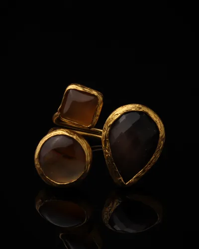 Nutmeg & Soot - a gold-plated ring with three brown and black cat eye stones, on black